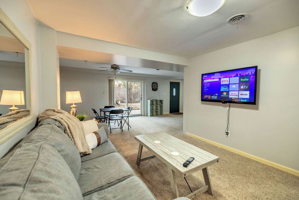 A living room with a grey sofa, a wooden coffee table, and a TV mounted on the wall displaying streaming services.