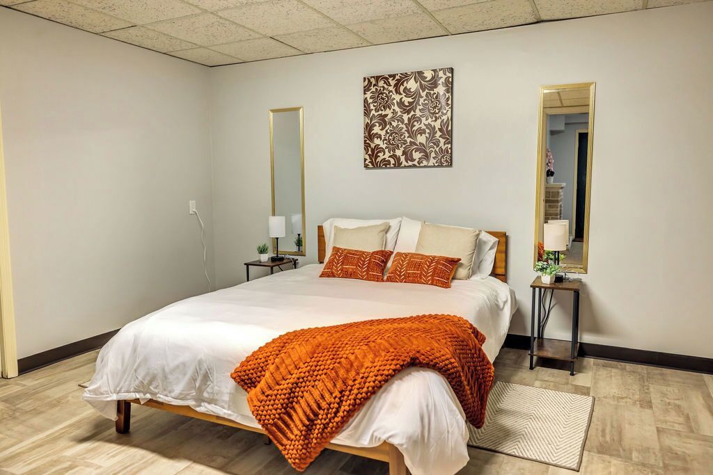 A neatly arranged bedroom with a large bed, two bedside tables, a mirror, and a decorative wall piece.