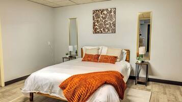 A neatly arranged bedroom with a large bed, two bedside tables, a mirror, and a decorative wall piece.