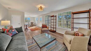 A spacious living room with a gray sofa, beige armchair, and a glass coffee table. There is a wooden bookshelf and a dining area in the background. - Morris Ranch (Fredericksburg)