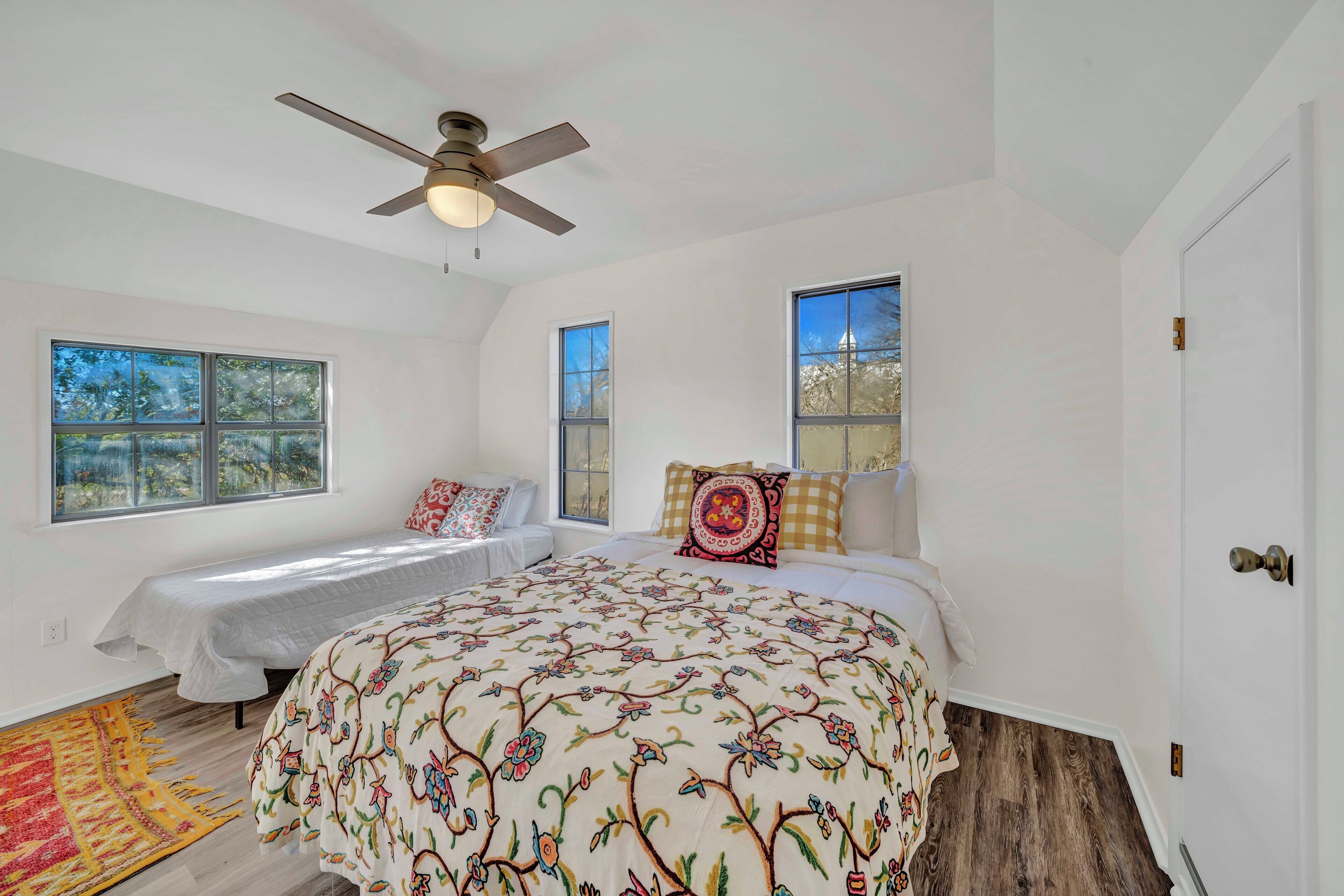 A bedroom with a bed, two windows, a ceiling fan, and a door.