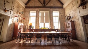 A spacious dining area with a long wooden table and chairs, large windows, stone walls, and various hunting trophies. - Morris Ranch (Fredericksburg)