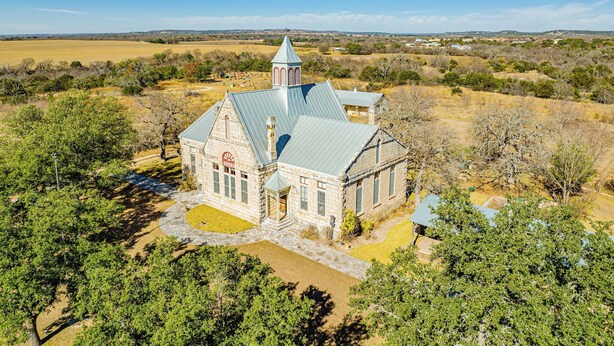 A stone church with a steeple, surrounded by trees and fields. - Morris Ranch (Fredericksburg)