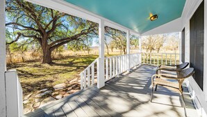 A covered porch with white railings and a bench, overlooking a grassy area with trees. - Morris Ranch (Fredericksburg)