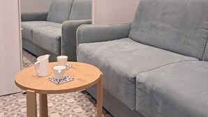 Een moderne kamer met een grijze bank, een klein houten tafeltje met kopjes en een karaf, en een vloer met een geometrisch patroon.