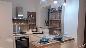 Een moderne keuken met een inbouwoven, een koffieapparaat en een eethoek met een houten tafel en stoelen.