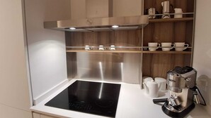 Een moderne keuken met een ingebouwde kookplaat, een koffieapparaat en planken met bekers en een waterkoker.