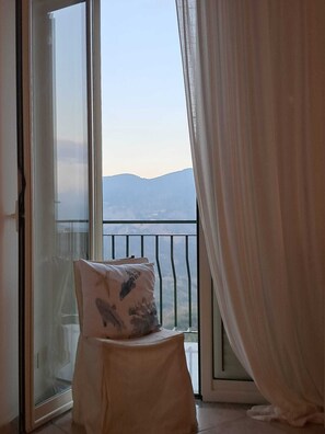 A balcony with a view of distant mountains, a chair with a cushion, and sheer curtains. - Dolce-Vista, Spacious 3 Bed Apartment with Panoramic Views (Isnello)