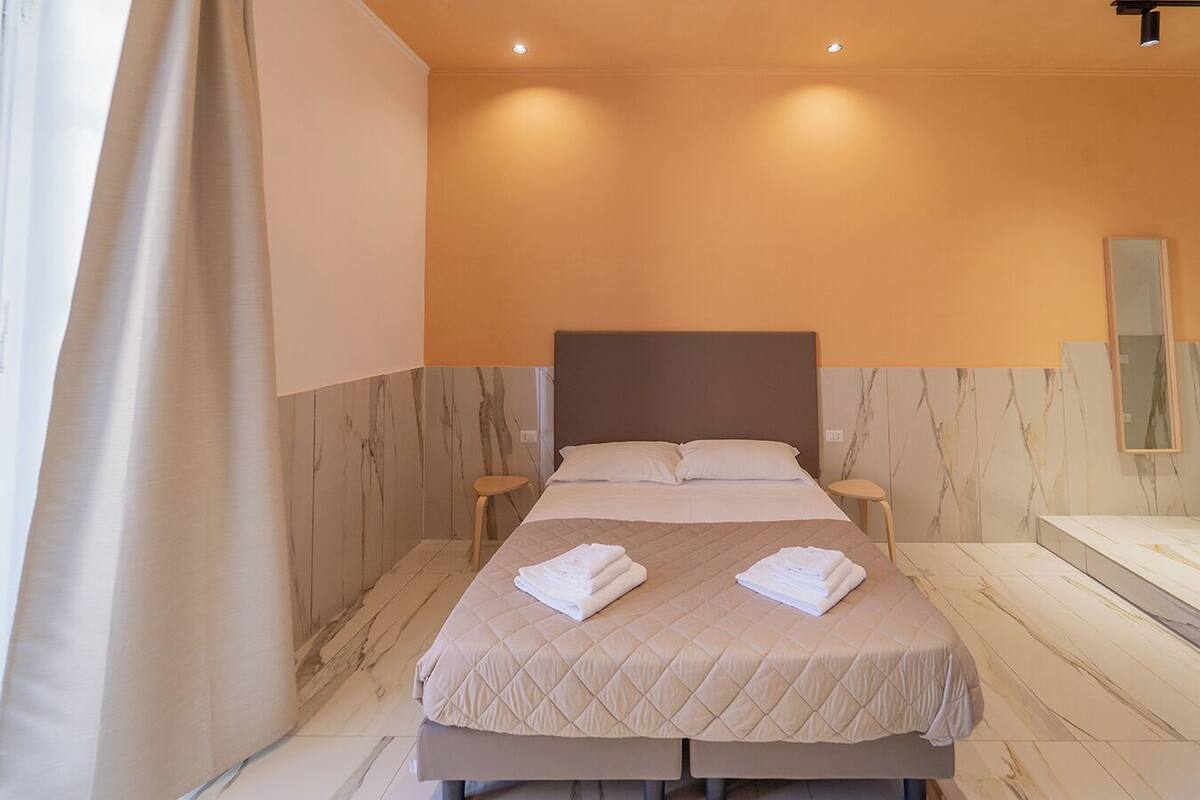 Hotellihuone, jossa on sänky, kaksi yöpöytää, suuri peili ja kylpyammeella varustettu kylpyhuone.