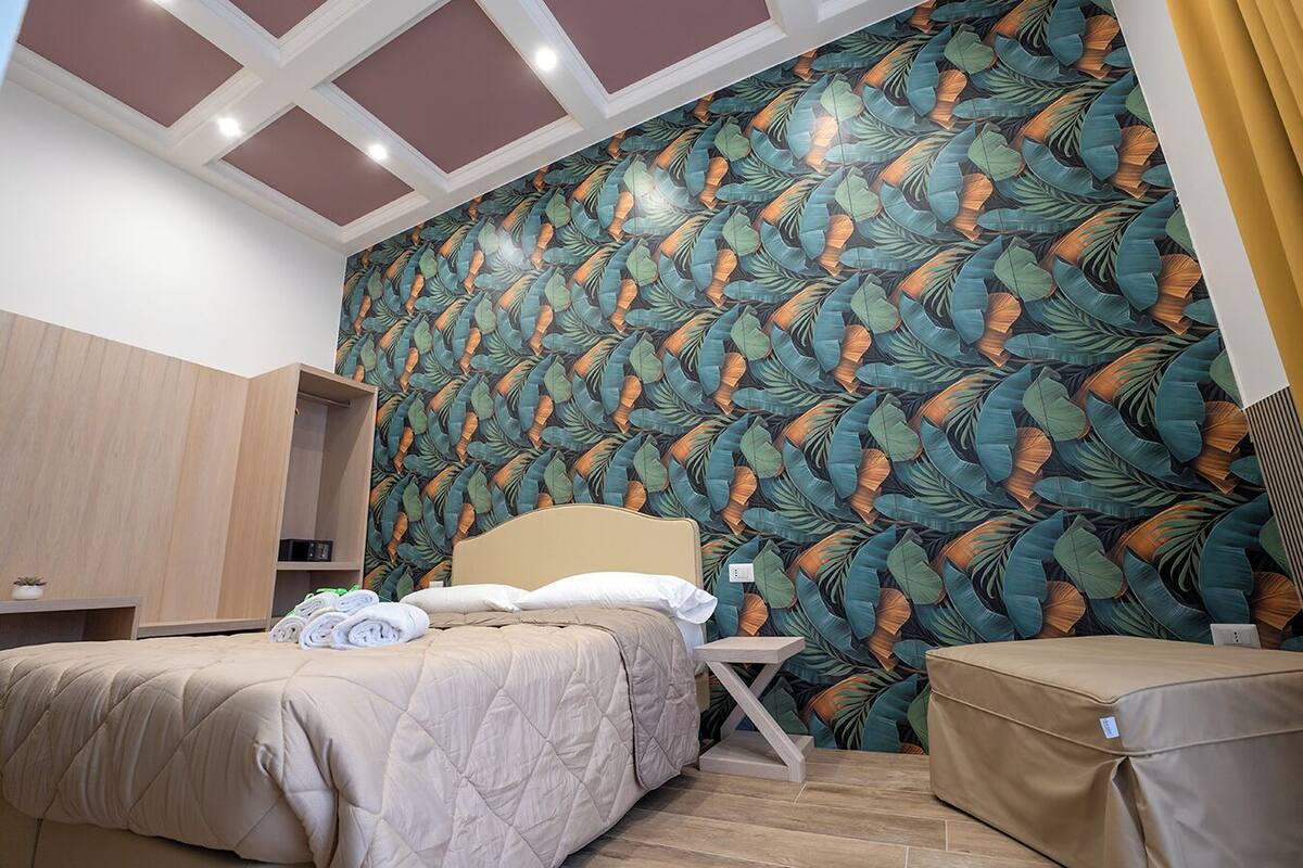 Hotellihuone, jossa on sänky, yöpöytä, vaatekaappi ja suuri ikkuna, jossa on verhot.