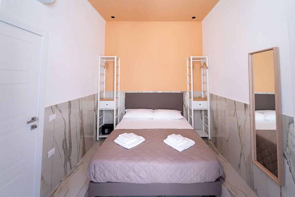 Hotellihuone, jossa on sänky, kaksi yöpöytää, vaatekaappi, peili ja marmorikuvioidut seinät.