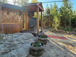 A wooden cabin with a porch and a stone wall. There are two wooden planters with plants.