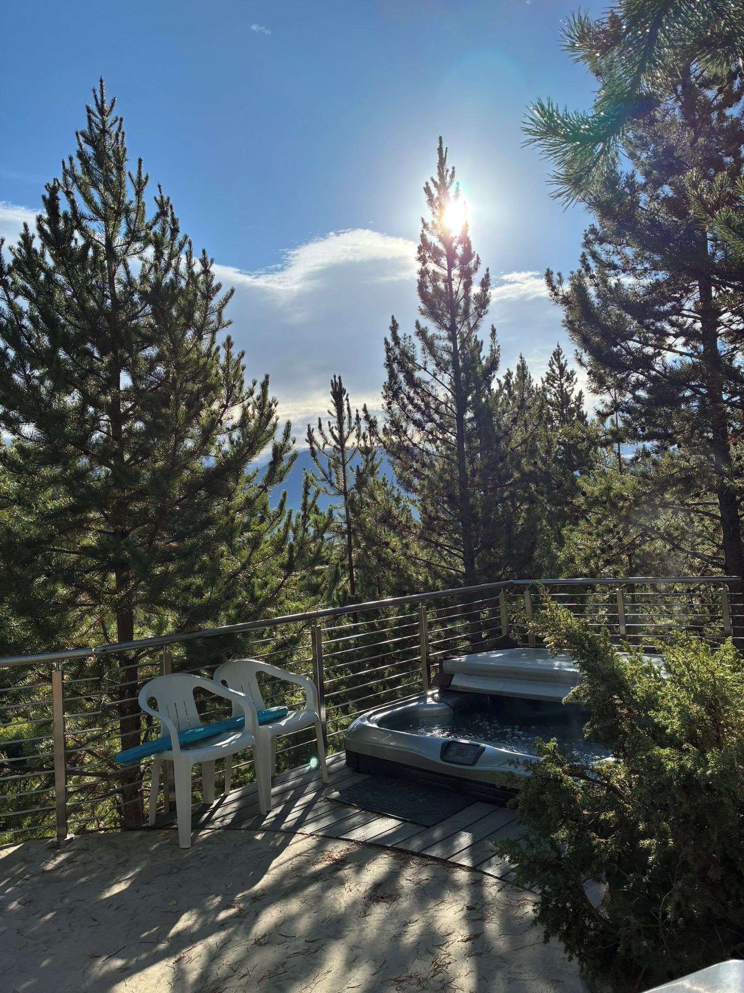 Une terrasse dotée d’un jacuzzi, d’une chaise et d’une rambarde offrant une vue sur une zone boisée.