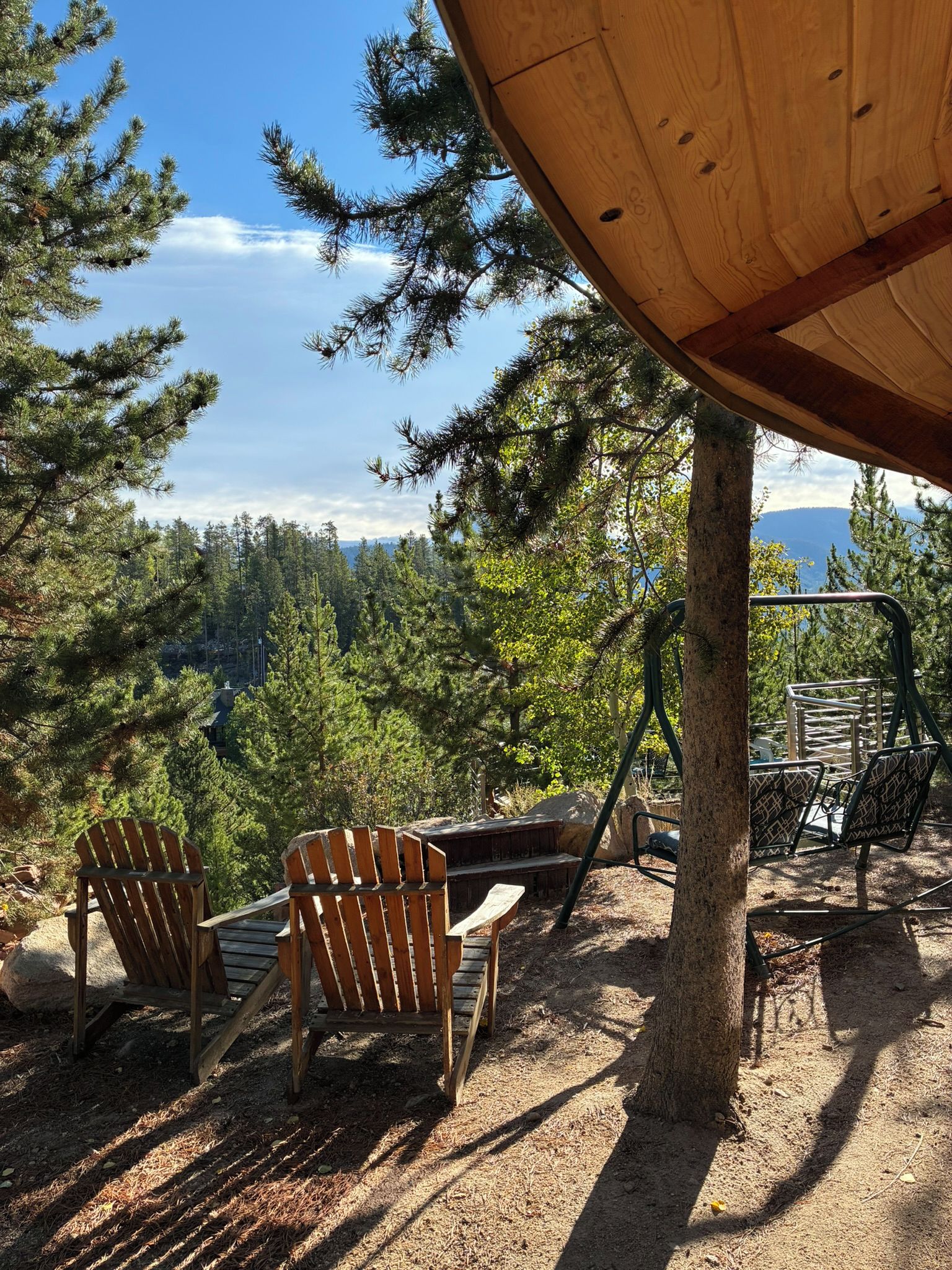 A wooden deck with Adirondack chairs, a metal railing, and a view of a forested landscape.