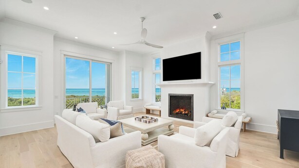 Un salón espacioso con mobiliario blanco, chimenea y grandes ventanales con vistas al océano.