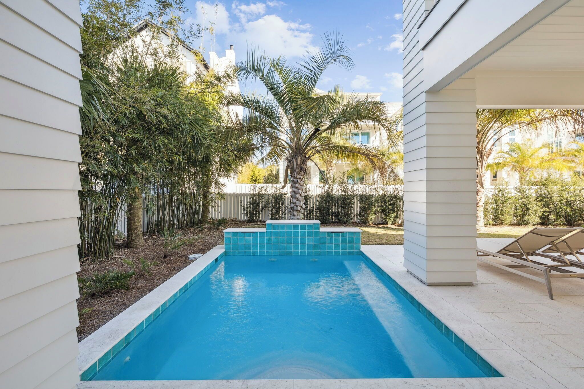 A swimming pool with a tiled edge, surrounded by a white fence and various plants.