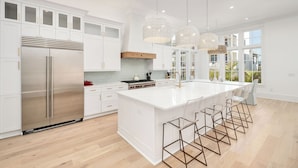 Una cocina moderna con armarios blancos, un refrigerador de acero inoxidable, una isla grande con taburetes de bar e iluminación colgante.