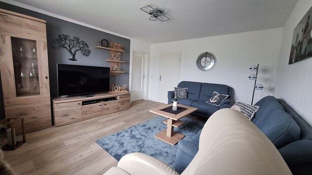 A modern living room with a flat-screen TV, wooden entertainment unit, blue sofa, and a small coffee table. - Cozy vacation apartment for 2 people - only 15 minutes to Boltenhagen (Upahl)