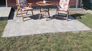 A brick house with a red-tiled roof, a window, and a patio with two wooden chairs and a small round table. - Cozy vacation apartment for 2 people - only 15 minutes to Boltenhagen (Upahl)