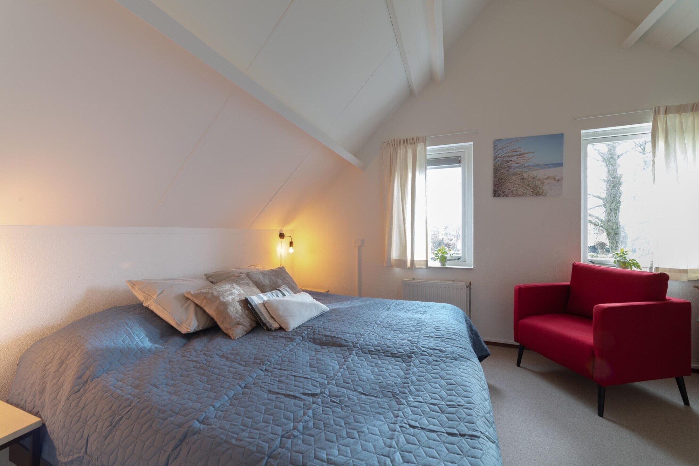 A bedroom with a large bed, a red chair, and a window with curtains.