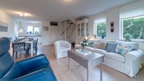 Una sala moderna con comedor, muebles blancos, una escalera y ventanas amplias.