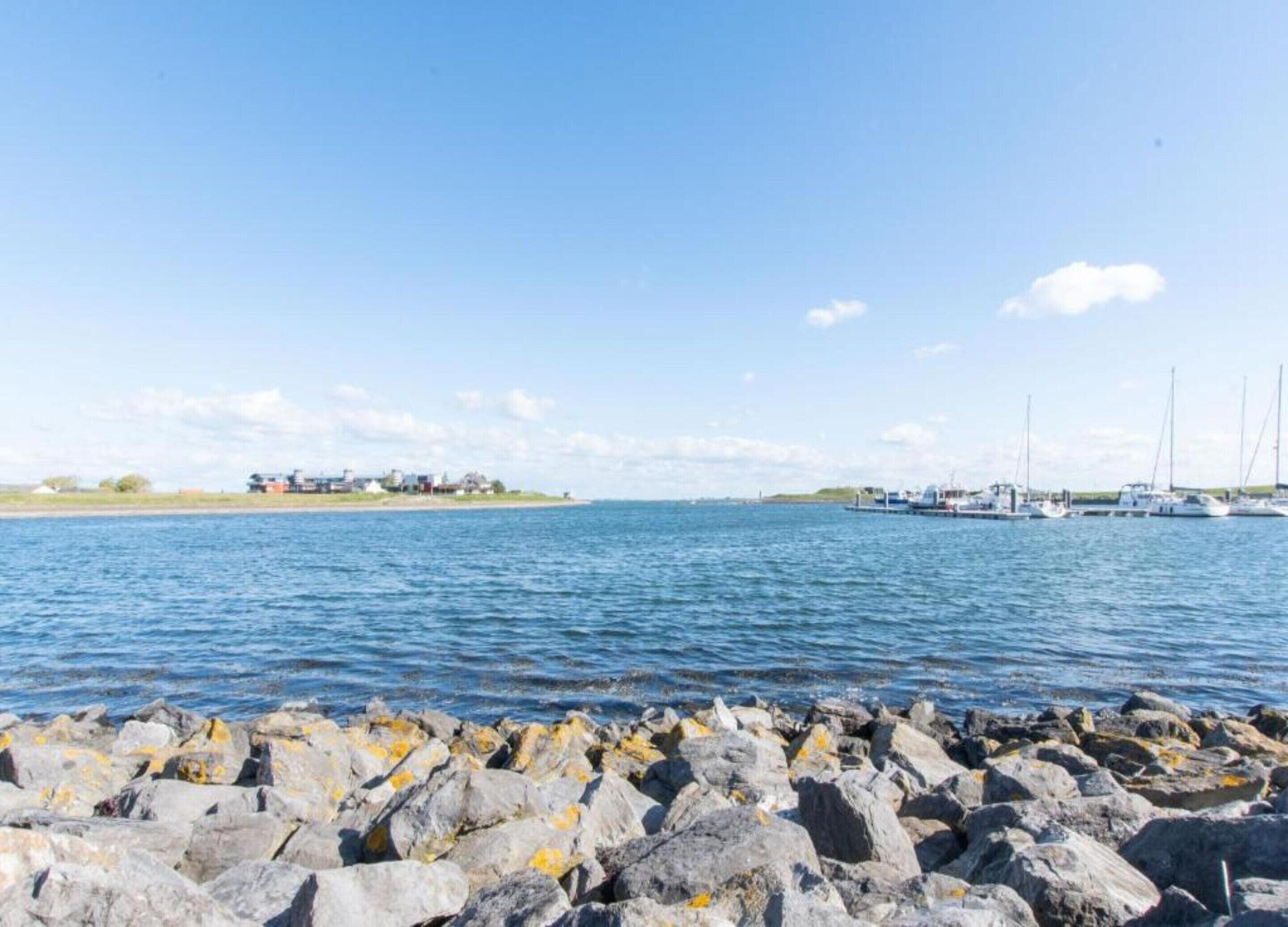 Eine Küstenlandschaft mit felsiger Küste, einer kleinen Insel mit Gebäuden und mehreren Segelbooten auf dem Wasser.