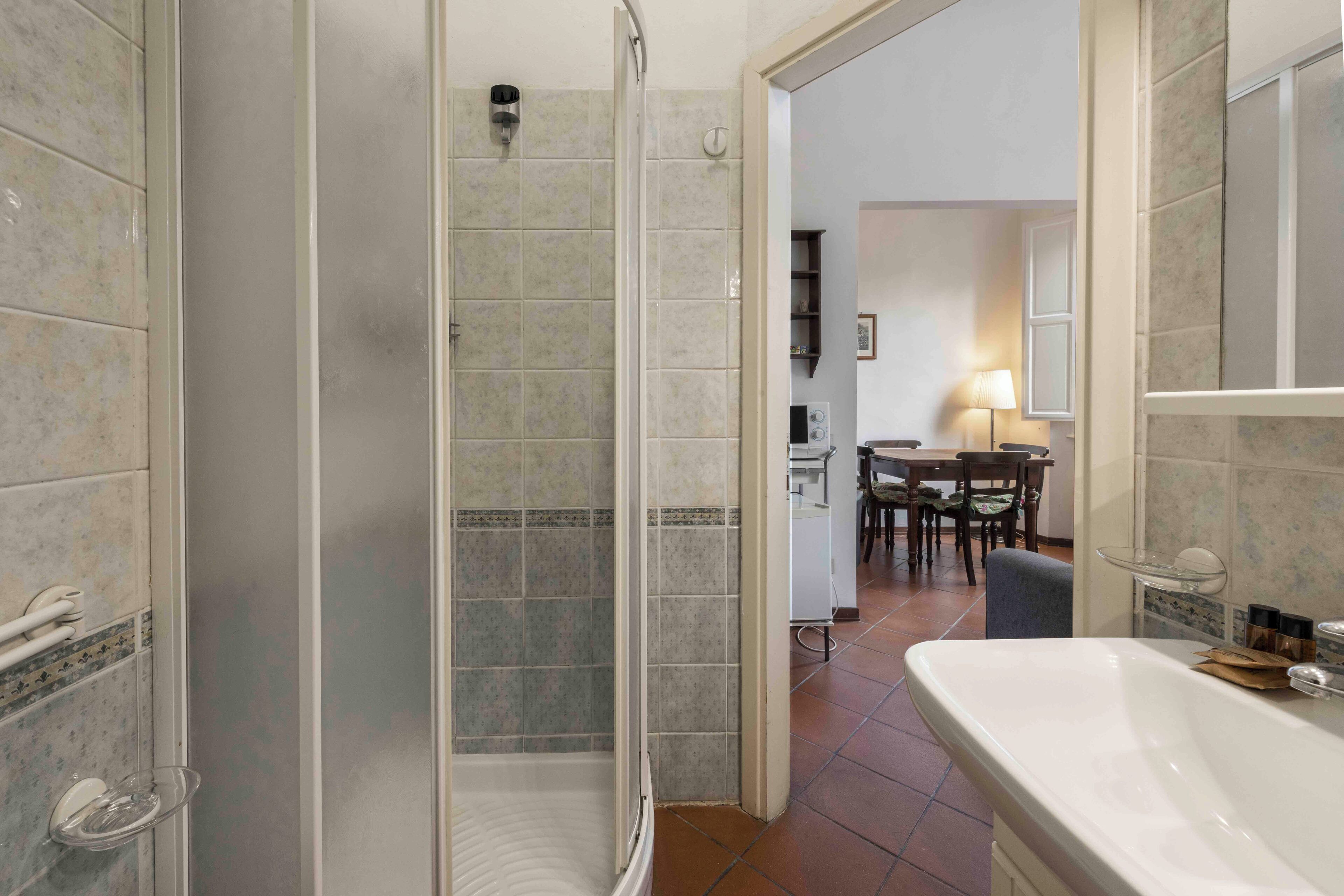 A bathroom with a glass shower enclosure, a white bathtub, and a tiled floor.