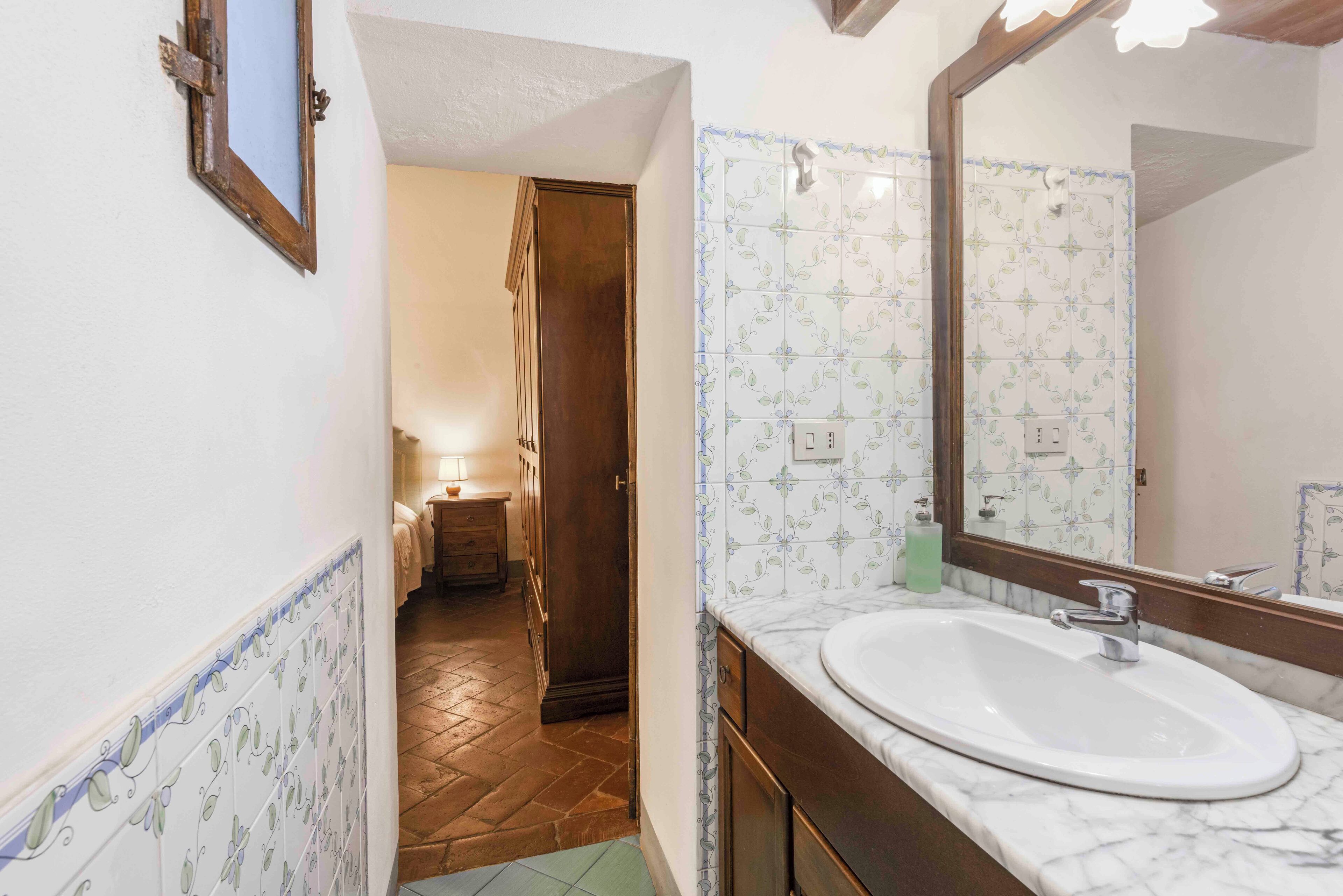Un baño con un lavabo blanco, un espejo y baldosas estampadas.