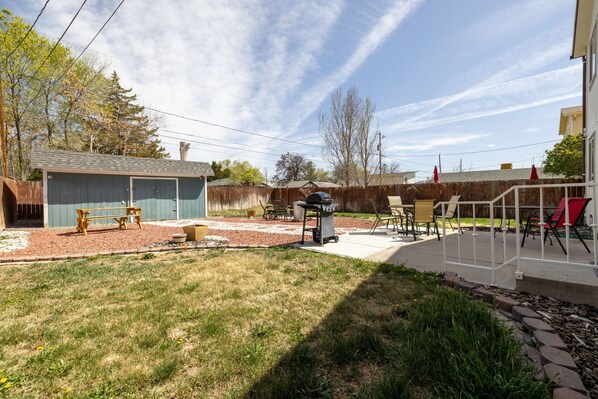 A backyard with a barbecue grill, outdoor seating, and a shed.