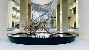 Un atrio moderno con una escultura geométrica única en el centro, rodeado de techos altos y un diseño limpio y minimalista.