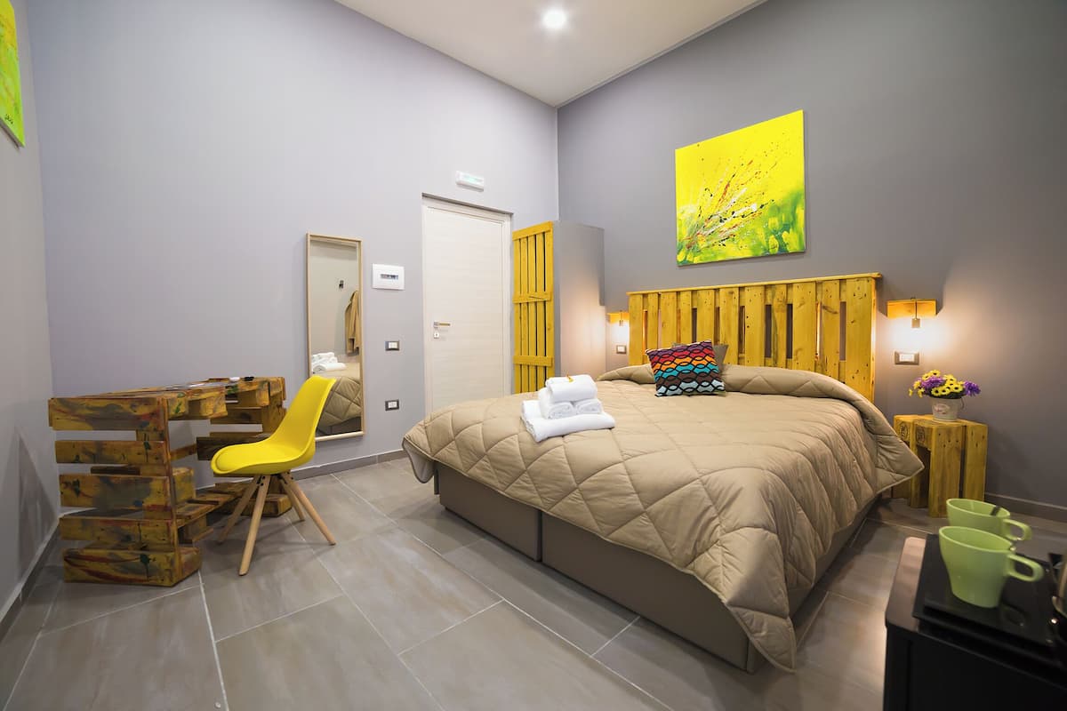 A bedroom with a bed, a desk, a chair, and a small table with a vase of flowers.