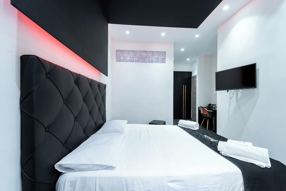 A modern hotel room with a large bed, a flat-screen TV mounted on the wall, and a small desk with a chair.