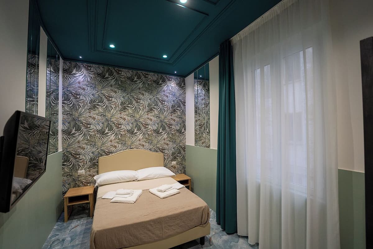 A bedroom with a bed, a nightstand, a mirror, and a window with curtains.