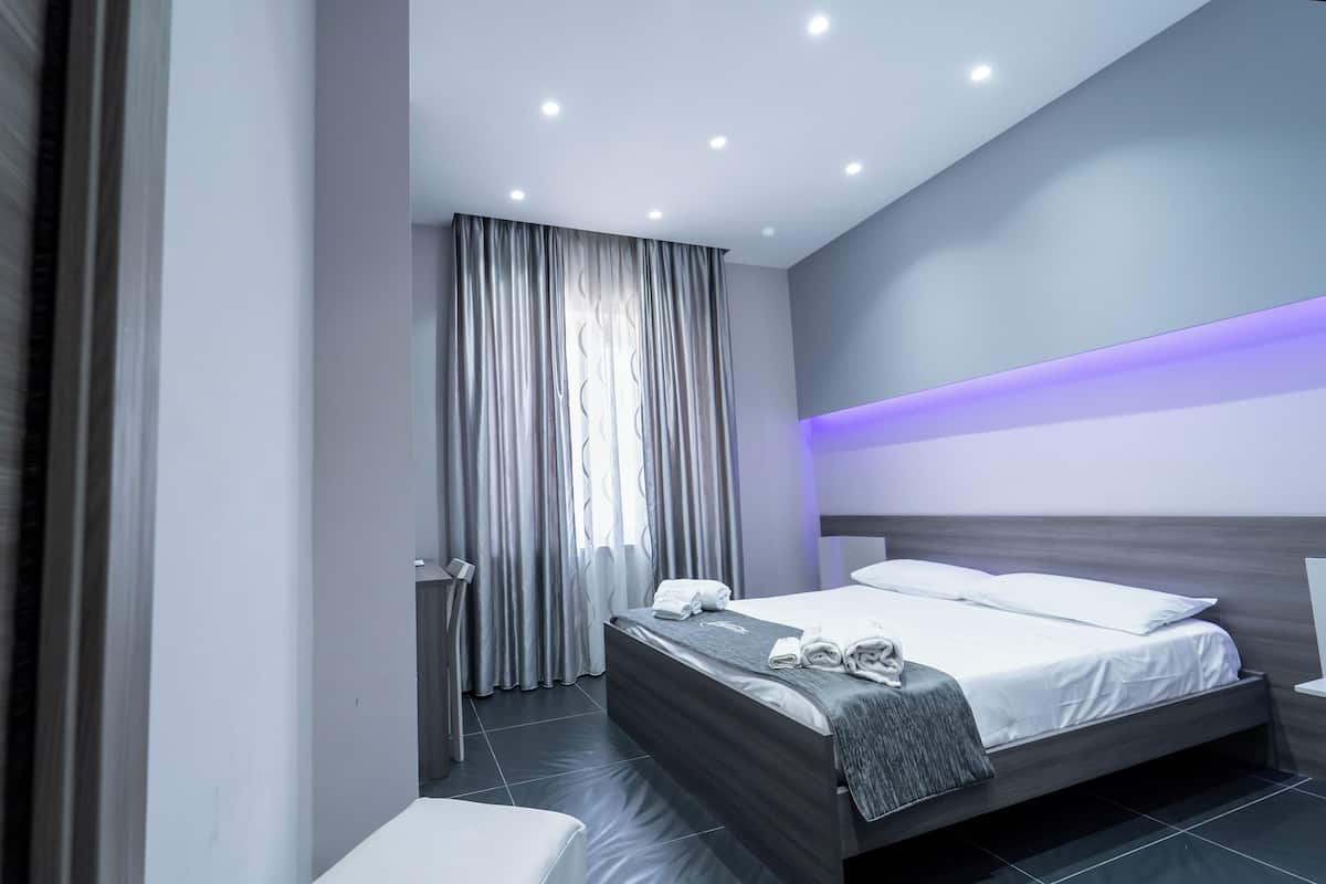 A modern hotel room with a bed, bedside table, and a large window with curtains.
