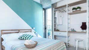 Un dormitorio con cama, mesita de noche, lámpara colgante, armario, escritorio, silla y planta en maceta.