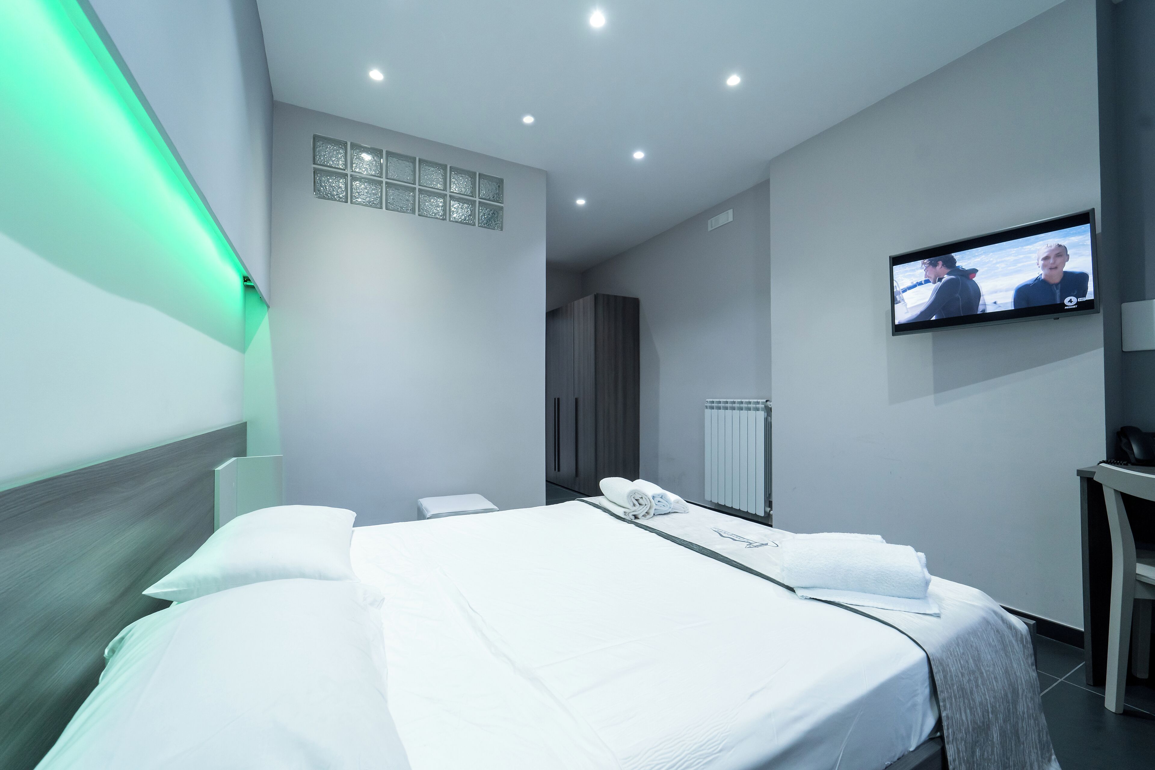 Una habitación de hotel moderna con una cama bien hecha, un televisor de pantalla plana en la pared y un escritorio pequeño.