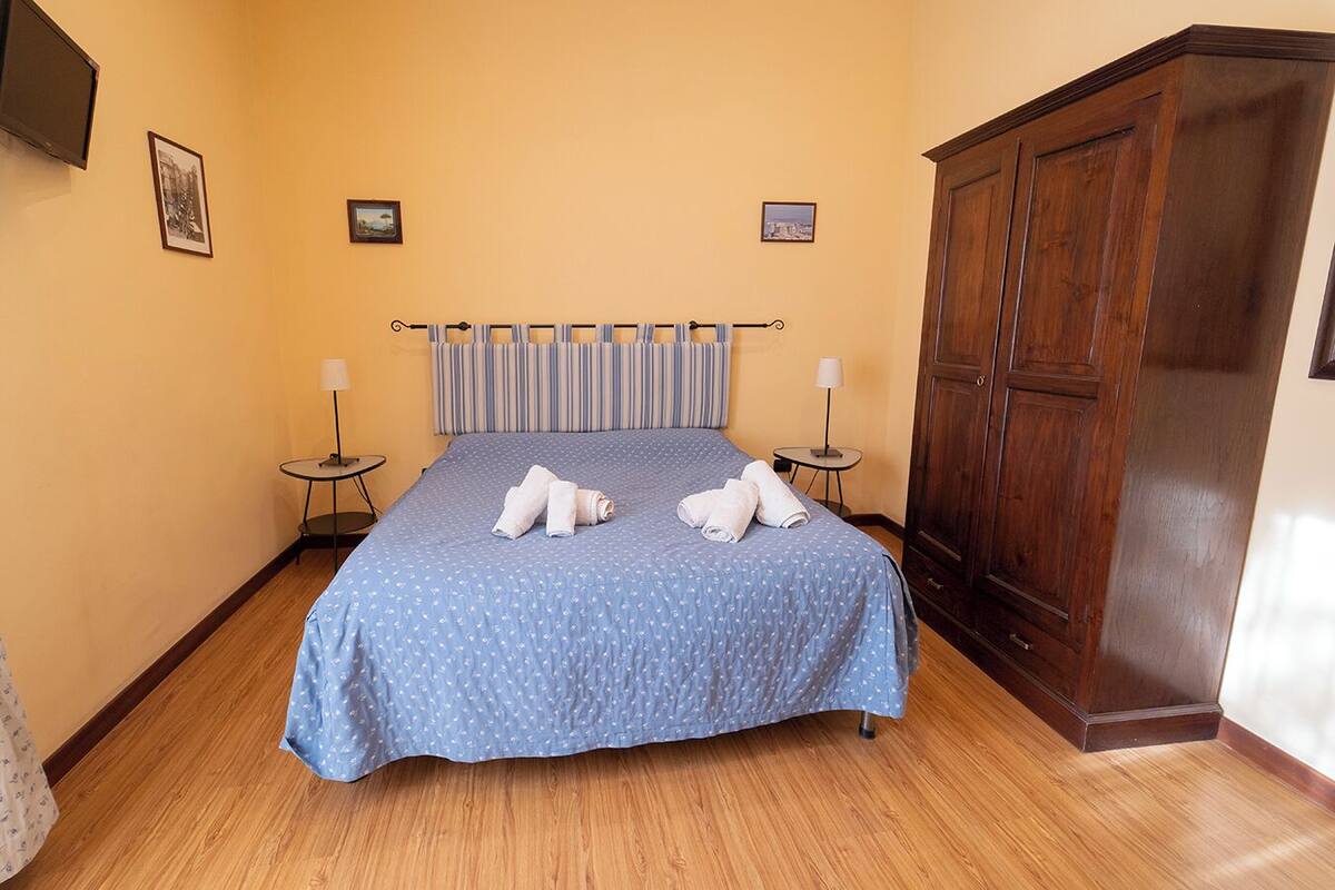 A neatly made bed with a blue bedspread and pillows, two bedside tables with lamps, and a wooden wardrobe.