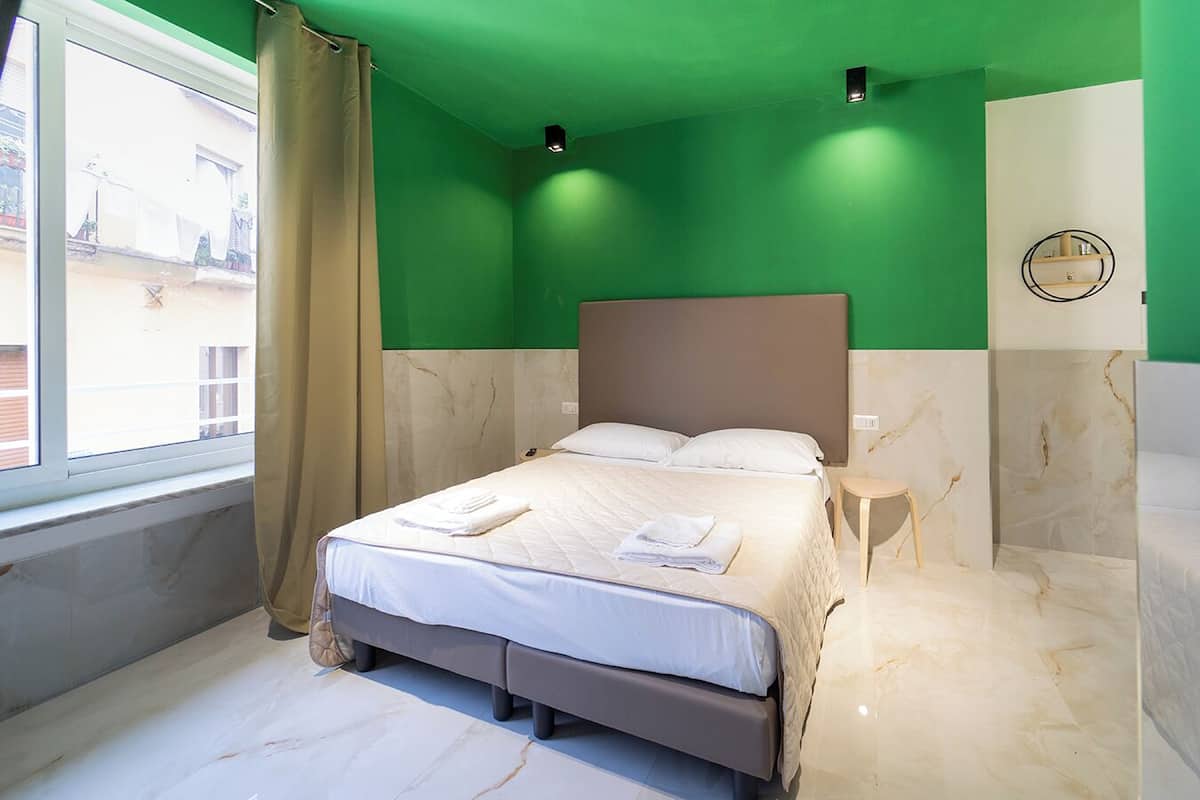 A bedroom with a bed, a chair, a window, and a green wall.