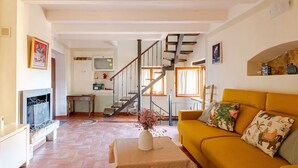 A living room with a sofa, a fireplace, a staircase, and a kitchen area.