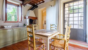 A rustic kitchen with a wooden table and chairs, a built-in oven, and a window with curtains.