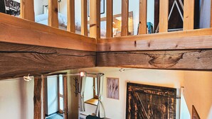 Un loft espacioso con techo alto, vigas de madera a la vista, un sofá azul con cojines estampados y una puerta de madera rústica.