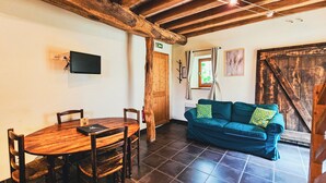 Una habitación acogedora con una mesa y sillas de madera, un sofá azul con cojines y un techo rústico con vigas de madera.