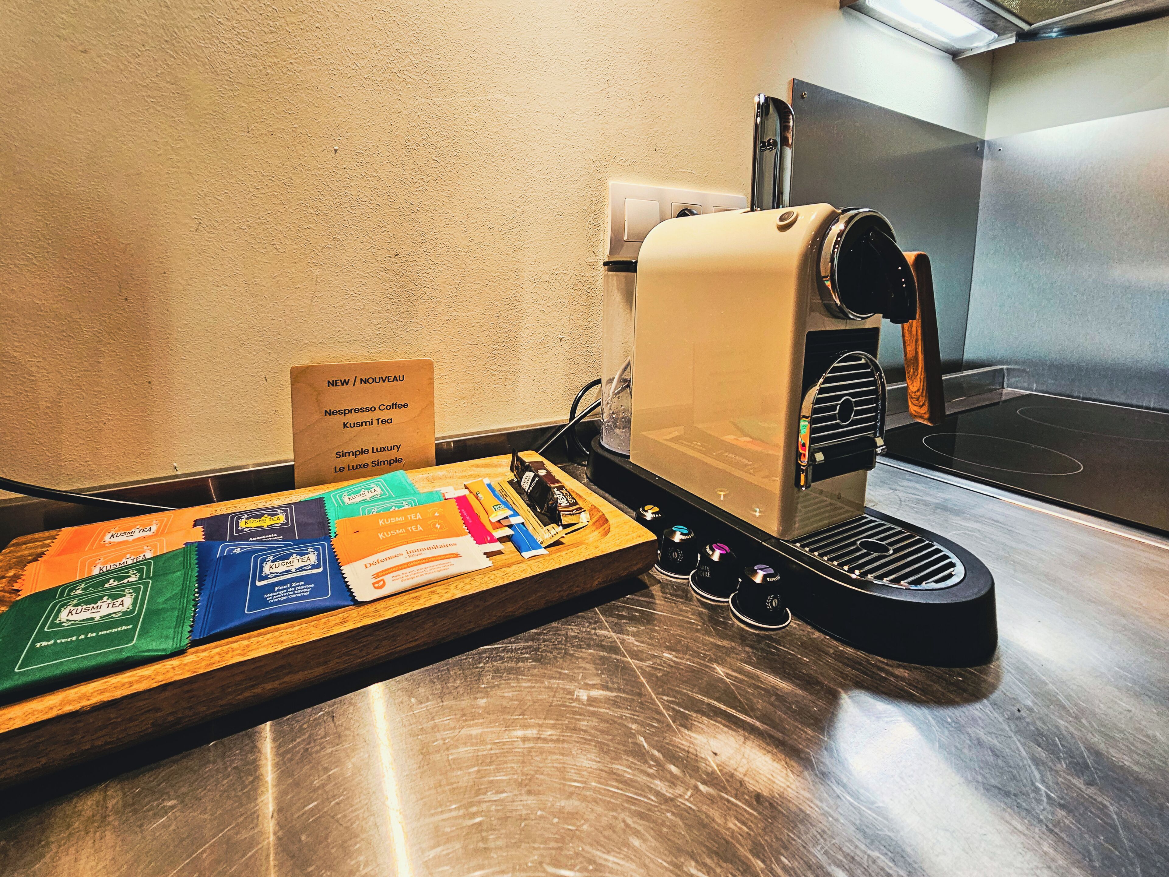 Une machine à café avec un assortiment de dosettes de café disposées sur un plateau, un panneau indiquant les nouveaux produits ou les nouveautés, et un comptoir en acier inoxydable.