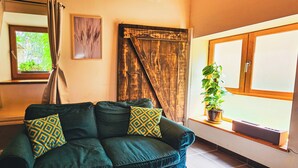 Un sofá color turquesa con cojines estampados, una puerta de madera, una ventana con una planta y una obra de arte enmarcada en la pared.