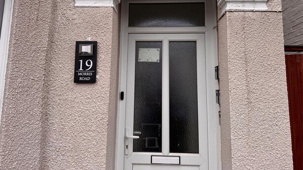 Una casa con el número 19 en una pared texturizada, una puerta blanca con un panel de vidrio y un buzón debajo.