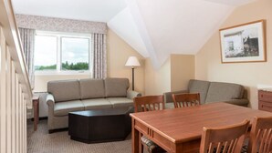 A cozy room with a sofa, a dining table, and chairs. There is a window with curtains, a lamp, and a framed picture on the wall. - Ski-In 2BR Loft | Sleeps 8 (West Dover)