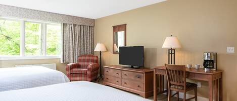 Habitación de hotel con dos camas, televisión, escritorio con silla y cafetera.