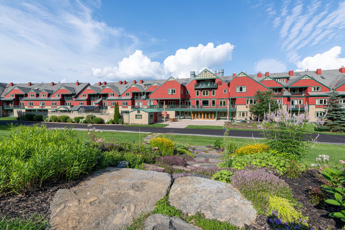 A row of red-roofed buildings with a central green-roofed structure, surrounded by landscaped gardens and large rocks.