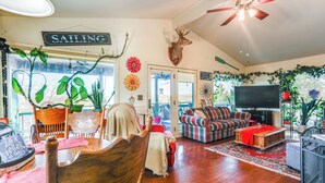 A cozy living room with a wooden floor, a sofa, a television, and a ceiling fan. - 'The Treehouse' in Cherokee Village: Deck & Views (Cherokee Village)
