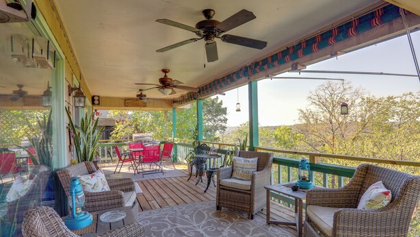 A covered outdoor seating area with wicker furniture, ceiling fans, and a view of trees. - 'The Treehouse' in Cherokee Village: Deck & Views (Cherokee Village)